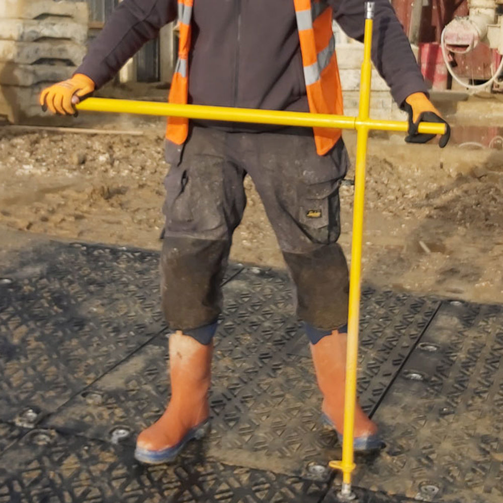 Person in work attire holding a yellow pole on a construction site