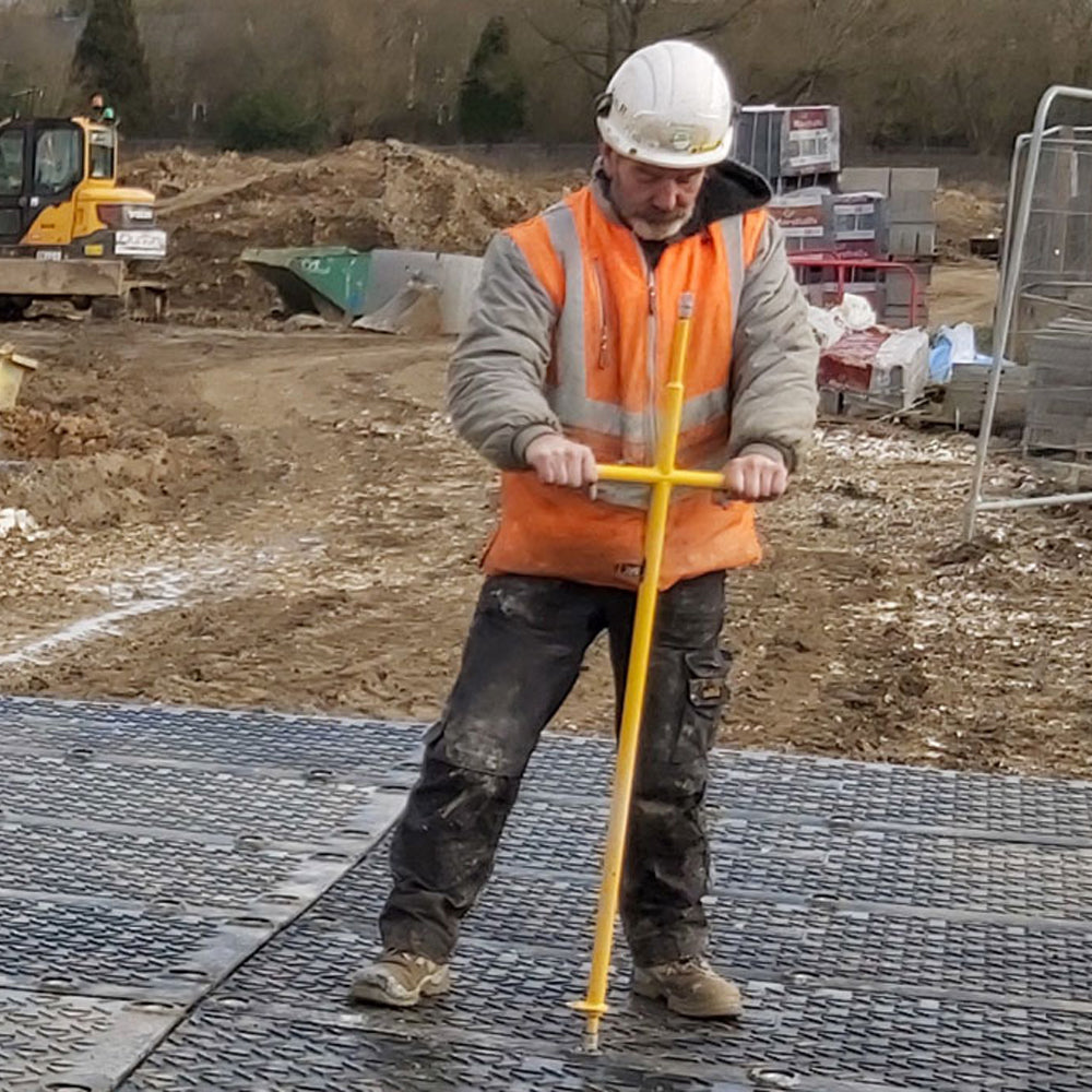 Person in safety gear using a yellow tool on a construction site